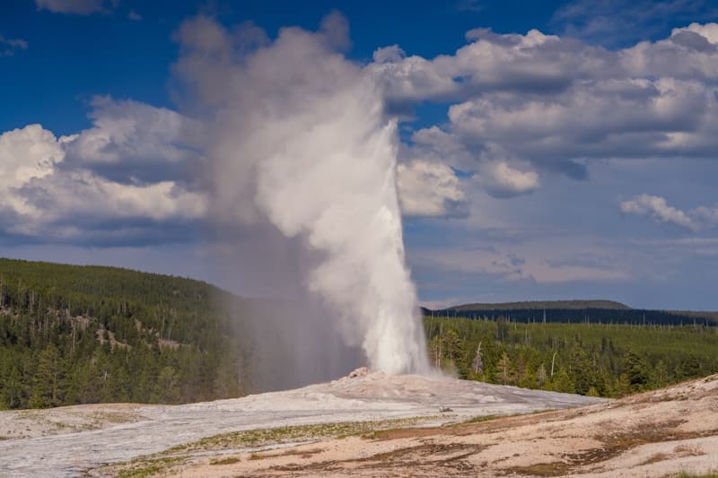 Old Faithful geyser erupting against blue sky