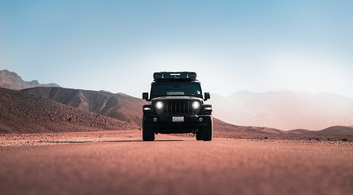 Jeep driving down a desert road with mountains in the background